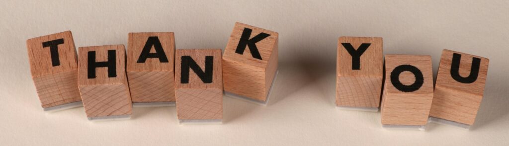 Wooden blocks spell 'THANK YOU' on a soft beige background, expressing gratitude.